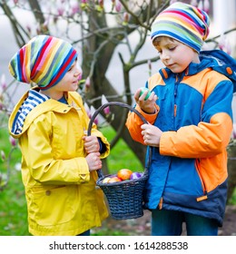 Two little kids boys and friends making traditional Easter egg hunt in spring garden, outdoors. Siblings having fun with finding colorful eggs. On cold day. Old christian and catholoc tradition.