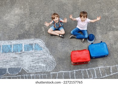 Two little kids boys having fun and train picture drawing and colorful chalks asphalt  Children having fun and chalk   crayon painting  going vacations   travel  Friends and suitcases