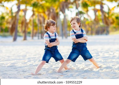 Two little kids boys having fun on tropical beach, happy best friends playing, friendship concept. Siblings brothes in family look with palms on background. Miami Florida USA
