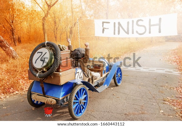 Two little kids in the\
guise of a racer and mechanic on old race car finish competitions\
in autumn park