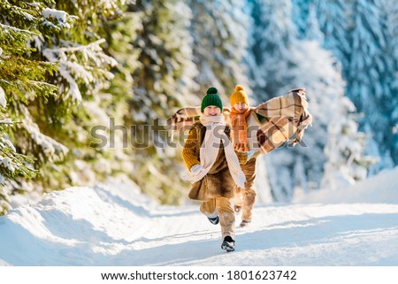 Two little kids have fun in the beautiful winter nature with snow-covered Christmas trees. Children run along a snowy road. Winter knitted wool retro clothes.
