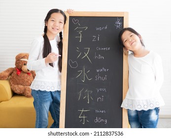 Two little kids standing by blackboard happy writing Chinese text. Young Asian small girls study together at home easy learning Chinese language, write on chalkboard. Homeschooling children lifestyle.