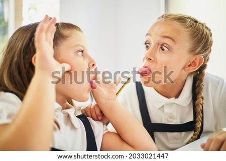 Two little school girls making mockery to each other in class