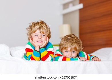 Two little sibling kid boys having fun in bed after sleeping at home, indoor. Brothers smiling at the camera.