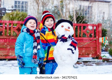 Two Little Siblings Boys Making A Snowman. Kids Playing And Having Fun With Snow, Outdoors  On Cold Day. Active Outdoors Leisure With Children In Winter.