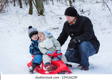 Two Little Siblings And Their Father Having Fun On Sledge On Winter Snow Day