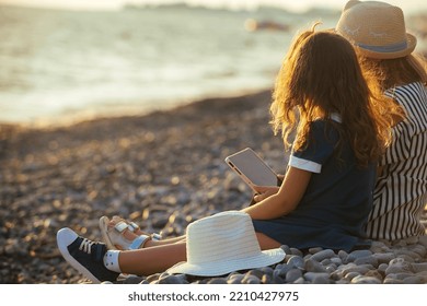 Two Little Sister Girls Are Sitting On The Seashore At Sunset. Family Travel During Holidays