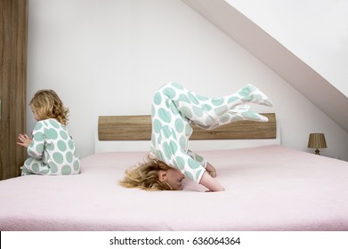 Two Little Sisters Twins Actively Have Fun On Their Parents' Beds, Children In Pajamas Light, Morning Photography.Jump, Tumbling, Standing On The Head,