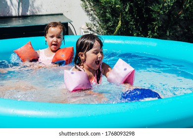 Two Little Twin Girls Wearing Muffs Bathe In A Pool In Summer