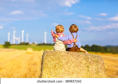 Two little twin kids boys sitting on hay stack or bale and speaking on yellow wheat field in summer. Children having fun together. Active leisure for kids