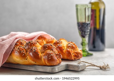 Two loaves of homemade Challah bread with pink cover, a glass of wine in background. Light grey background. Selective focus. Copy space.