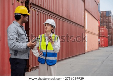 Two logistics engineers discussing work plan at container terminal. Female supervisor pointing up while male colleague checks data on digital tablet during cargo inspection at shipping port.