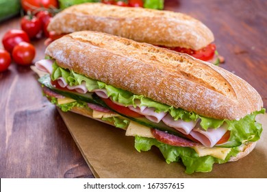 Two Long Ciabatta Sandwiches with lettuce, slices of fresh tomatoes, cucumber, ham, salami and cheese - Powered by Shutterstock