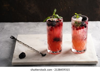 Two Long Glasses With Non-alcoholic Mocktail Version Of The Classic Blackberry And Gin Cocktail Bramble On Marble Board