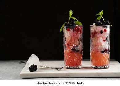 Two Long Glasses With Non-alcoholic Mocktail Version Of The Classic Blackberry And Gin Cocktail Bramble On Marble Board