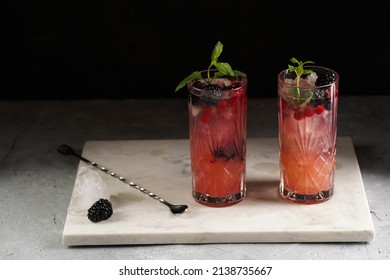 Two Long Glasses With Non-alcoholic Mocktail Version Of The Classic Blackberry And Gin Cocktail Bramble On Marble Board