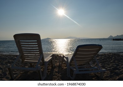 Two Lounge Chairs Facing The Sunset.