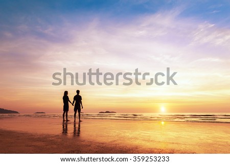 Two lovers standing together on a tropical beach and thinking about life, beautiful sunset in the background