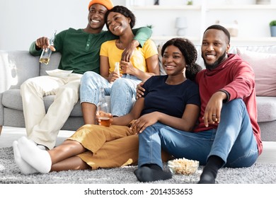 Two Loving Young Black Couples Watching Romantic Movie At Home, Having Double Date, Spending Weekend Together, Happy Millennials Drinking Beer And Enjoying Nice TV Show, Hugging And Smiling