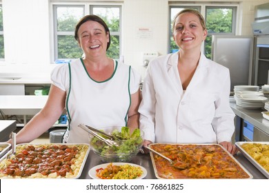 Two Lunch Ladies Standing Behind Full Lunch Service Station