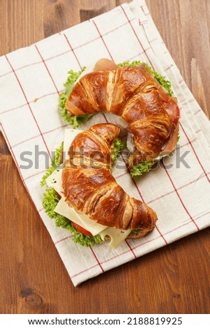 two lye croissant sandwiches with iberian ham, tomato slices, lettuce and cheese on marble board on wooden background