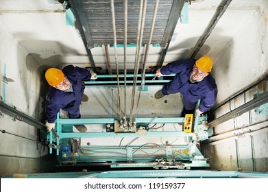 two machinist worker technicians at work adjusting lift with spanners in elevator hoist way