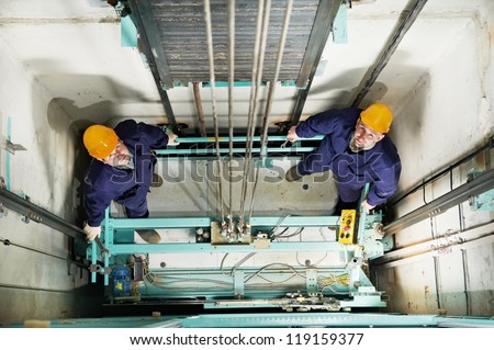 two machinist worker technicians at work adjusting lift with spanners in elevator hoist way