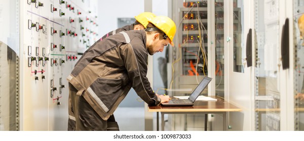 Two maintenance engineers inspect relay protection system with laptop computer. Bay control unit. Medium voltage switchgear