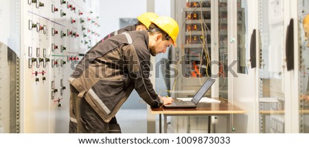 Two maintenance engineers inspect relay protection system with laptop computer. Bay control unit. Medium voltage switchgear