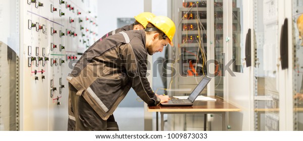Two\
maintenance engineers inspect relay protection system with laptop\
computer. Bay control unit. Medium voltage\
switchgear