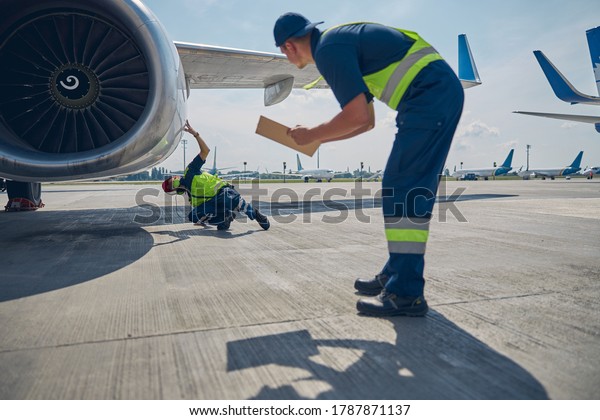 Two maintenance engineers\
performing a routine inspection of an air vehicle parked at the\
aerodrome