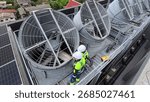 Two maintenance workers check large cooling towers on a commercial rooftop during the day.