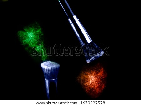 Two make up brushes with flying color powder, product on black background. Concept of glamour make up in minimal black