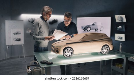 Two Male Automotive Designers Working On Eco Friendly Model Of Electric Car In Modern Car Design Studio. One Sculpting With Plasticine Clay, Other Working In 3D Modeling Computer Software.