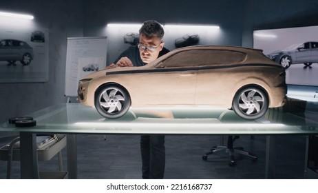 Two Male Automotive Designers Working On Model Of Eco Friendly Electric Car In Modern Car Design Studio. One Working In 3D Modeling Computer Software, Other Sculpting With Plasticine Clay And Rake.