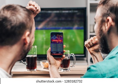 Two male buddies watching live football game broadcast tv   celebrating money win after making bets online at bookmakers website 