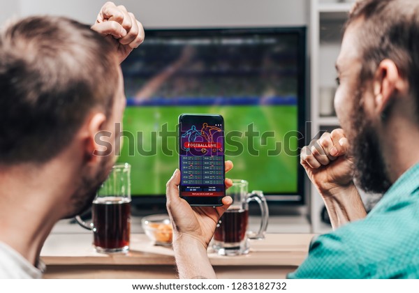 Two male buddies watching live football game\
broadcast on tv and celebrating money win after making bets online\
at bookmakers website.