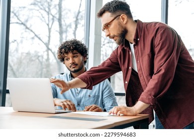 Two male business partners of different nationalities, concentrated work in a creative modern office, brainstorming on a new project, discussing ideas and strategy, analysing financial profit - Shutterstock ID 2279594683