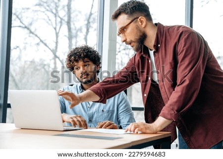 Two male business partners of different nationalities, concentrated work in a creative modern office, brainstorming on a new project, discussing ideas and strategy, analysing financial profit