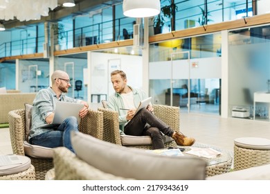 Two Male Business Partners Meeting In Office Lobby And Talking. Software Engineer With Open Laptop Explaining It Project While Manager Taking Notes In Notepad. Businessmen Working In Team