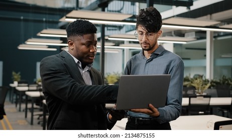 Two Male Business Partners Men Arabian Man Holding Laptop Showing Presentation African Businessman Looking At Computer Screen Colleagues Working Online Discuss Startup Pointing Display Making Choice