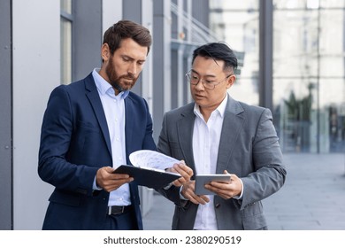 Two male business partners outside office clock discuss financial tasks and results, serious thinking businessmen discuss financial strategy, review contracts and reports. - Powered by Shutterstock