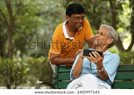 Two male elders using mobile phone in garden