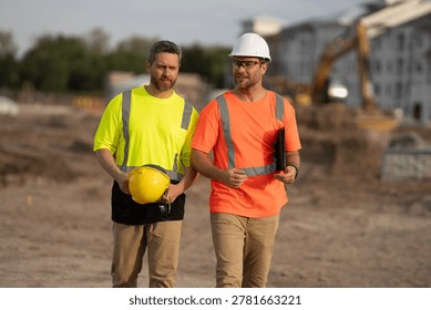 Two male engineers in protective helmets and reflective vests prepare to shake hands at construction site. Scene shows negotiation, mutual respect, professional communication, project and teamwork.
