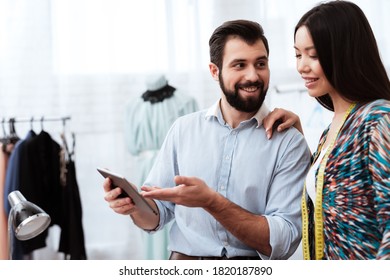 Zwei männliche und weibliche Modedesigner, die sich Tablet ansehen. Ein Mann mit Bart zeigt einem Mädchen etwas auf einem Tablett und lächelt. 