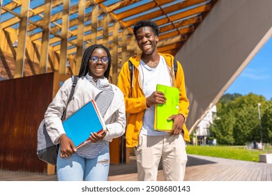 Two male and female young confident african american students walking together along the university campus carrying school bag and folders - Powered by Shutterstock