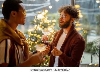 Two male friends celebrating winter holidays, standing together with wine at backyard. Christmas tree on background. Caucasian and hispanic man together. Idea of gay couples and holiday mood - Powered by Shutterstock