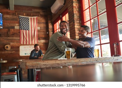 Two Male Friends Greeting One Another In Sports Bar Enjoying Drink Together