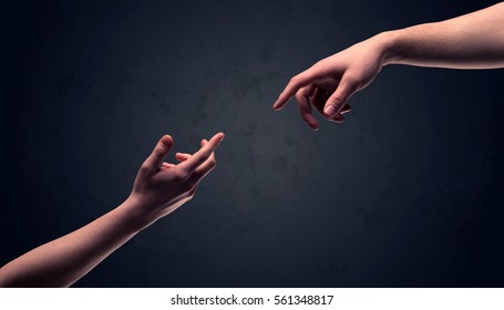 Two male hands reaching out to one another, almost touching, in front of dark clear empty background wall concept