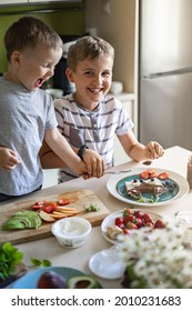 Two Male Little Friends Or Brother Decorating Morning Sandwich With Fruit, Berries And Chocolate Paste. Laughing Children Cooking Serving Funny Childish Food Together Having Fun And Positive Emotion